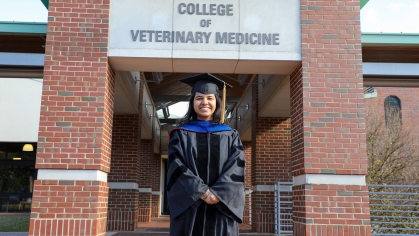 Ankita Gupta in graduation regalia standing under a sign that reads, 'College of Veterinary Medicine'.