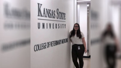 Caroline Pawlowski leaning against a wall that says, 'Kansas State University'.