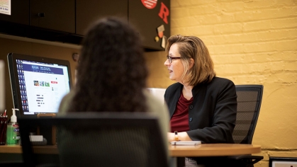 A dean at a desk talking to a student.