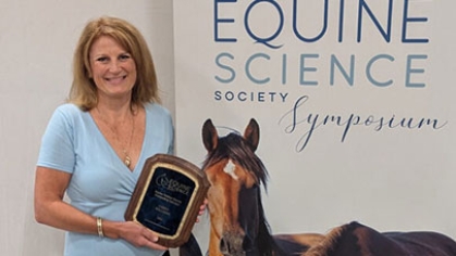 Carey Williams holding an award in front of a sign that says, 'Equine Science Society Symposium'.